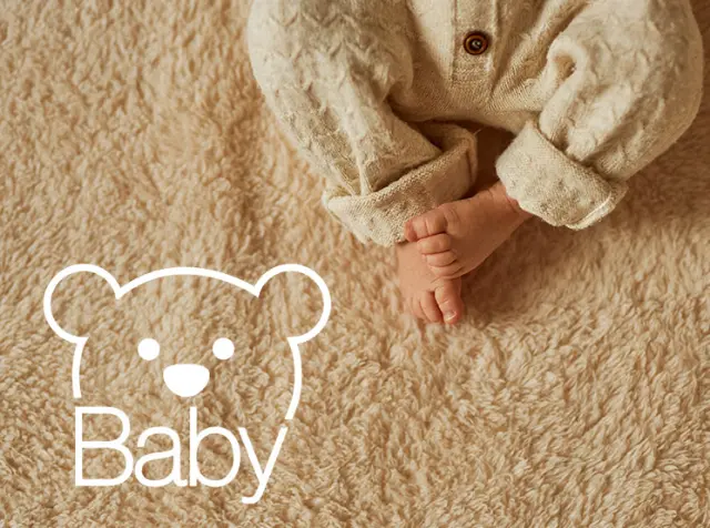 Babyfüße in hellbeigem Strampler auf weicher Decke mit weißem Teddybär-Logo und dem Wort „Baby“.